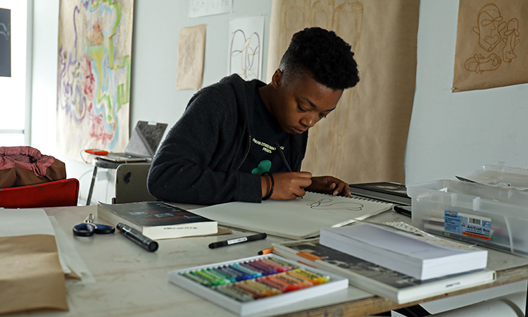 A student drawing at a table covered in drawing materials